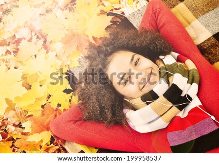 Enjoying Music in Nature. Latino American young girl lying on the dry leaves and listening to music