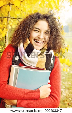Female student in warm autumn. Latino American young girl with books in hand on the background of the autumn landscape