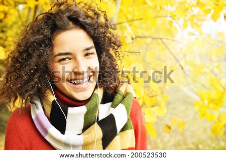 Female student in warm autumn. Happy Latino American young girl  listening to music on the background of the autumn landscape.