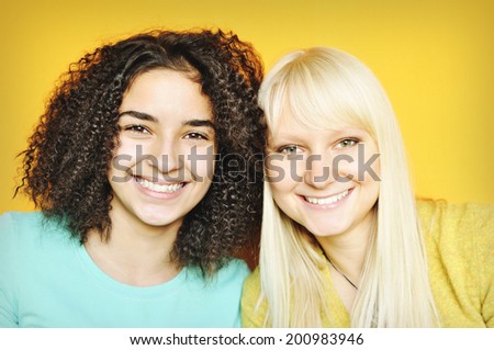 A pretty brunette with a pretty blonde girl isolated on yellow background.