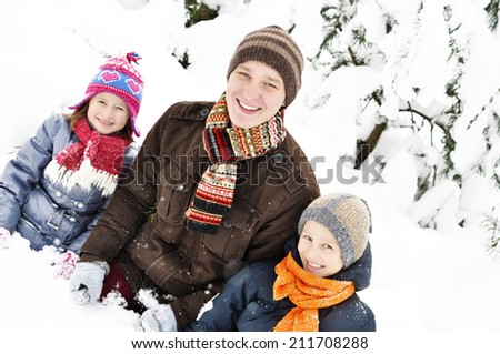 Happy family in the winter. Young father with two kids are sitting in the snow. It\'s snowing.