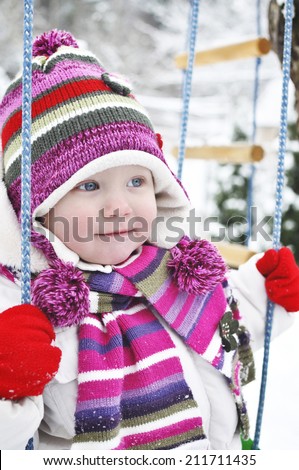 Happy Little girl in a winter garden. Pretty little girl sitting on a swing in the winter.