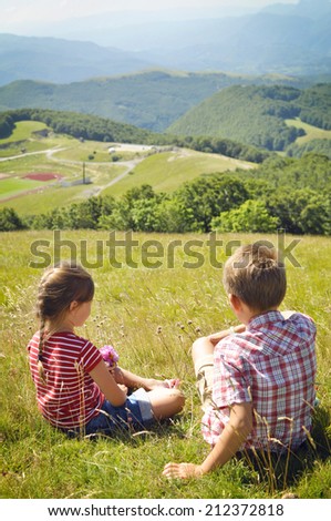 Kids hiking in the mountains. Little girl and boy sitting on the grass and looking at the Italian mountains.