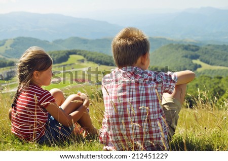 Kids hiking in the mountains in Italy.  Little girl and boy sitting on the grass and looking at the Italian mountains.