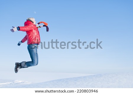 Pretty girl enjoys winter. Happy girl jumps up on the field in sunny winter day.