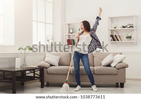 Happy woman cleaning home, singing at mop like at microphone and having fun, copy space. Housework, chores concept