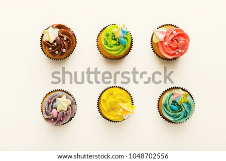 Top view on set of vanilla cupcakes with colorful buttercream tops isolated on white background. Tasty desserts in brown muffin liners. Delicious treats for birthday party, bakery concept, cutout
