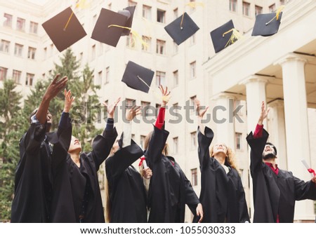 A group of multietnic students celebrating their graduation by throwing caps in the air. Education, qualification and gown concept.