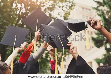 A group of multietnic students celebrating their graduation by throwing caps in the air closeup. Education, qualification and gown concept.