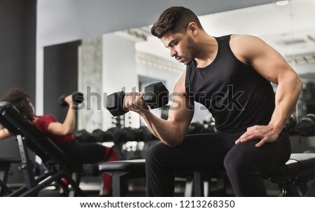 Arab muscular man doing biceps workouts with dumbbells in gym, copy space