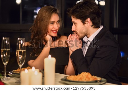 Handsome man kissing hand of his girlfriend in restaurant during romantic dinner