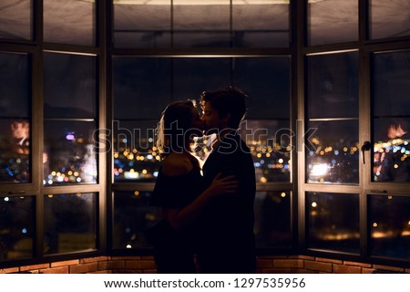 Couple in love kissing on panoramic window background overlooking nigth city.