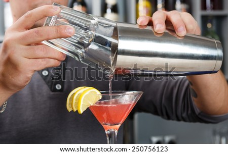 Barman\'s hands in bar interior mixing cosmopolitan cocktail
