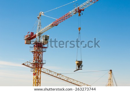 Tower crane lifting up a cement bucket at construction area against blue sky