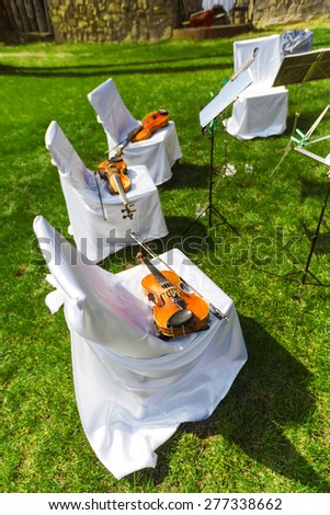 Outdoors wedding ceremony begins - string quartet\'s decorated festive chairs with violins