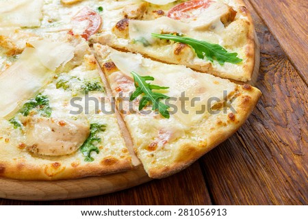 Delicious pizza with chicken, parmesan, tomatoes, white sause and fresh arugula - thin pastry crust at wooden background