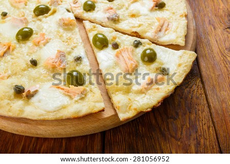 Delicious seafood pizza with salmon, capers and olives - thin pastry crust at wooden table background