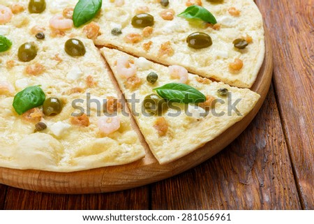 Delicious seafood pizza with shrimps, capers and olives - thin pastry crust at wooden table background