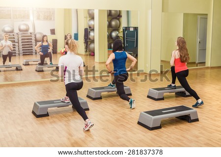 Group of young sportive women making step aerobics in the fitness class - back view