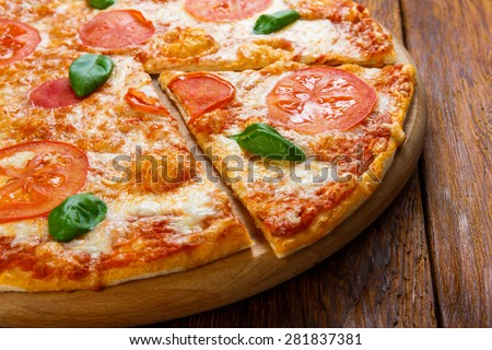 Delicious italian Margherita pizza decorated with basil leaves - thin pastry crust at wooden background
