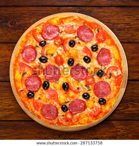 Delicious italian pizza with salami pepperoni, mushrooms and black olives - thin pastry crust at wooden table background, above view