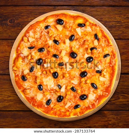 Delicious italian pizza with pineapple, chicken and black olives - thin pastry crust isolated at wooden background, above view