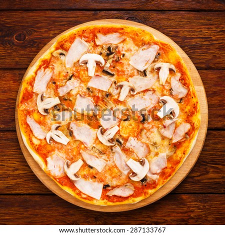 Delicious pizza with mushrooms and smoked chicken meat - thin pastry crust isolated at wooden background, above view