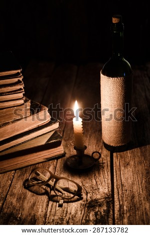 Vintage reading concept - pile of obsolete books, burning candle, wine and glasses at wooden table