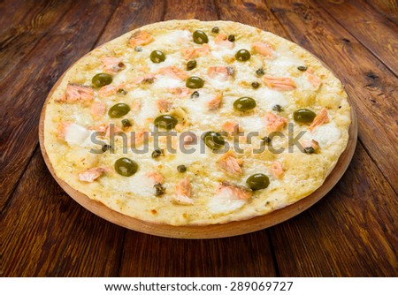 Delicious seafood pizza with salmon, capers and olives - thin pastry crust isolated at wooden background