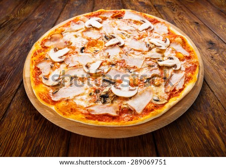 Delicious pizza with mushrooms and smoked chicken meat - thin pastry crust isolated at wooden background