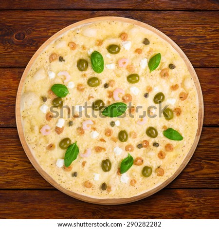 Delicious seafood pizza with shrimps, calamari rings, capers and olives - thin pastry crust at wooden table background, above view
