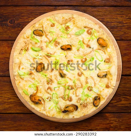 Delicious seafood pizza with shrimps, mussel, olives and leek - thin pastry crust at wooden table background, above view