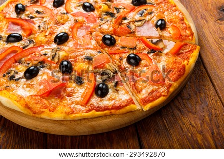 Delicious italian pizza with ham, peppers, mushrooms and black olives - thin pastry crust at wooden table background on wooden desk