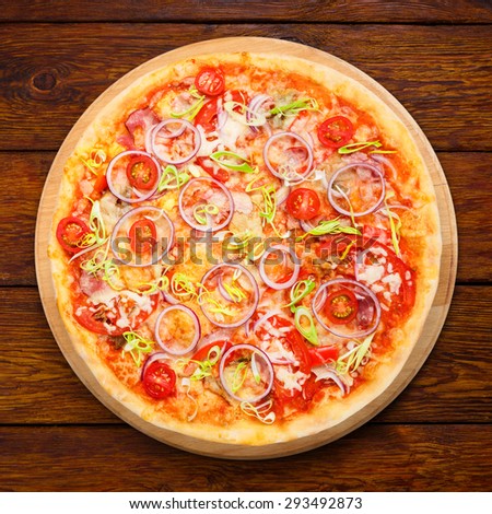 Delicious pizza with fresh onions, leek, bacon and cherry tomatoes - thin pastry crust isolated at wooden background above view on wooden desk