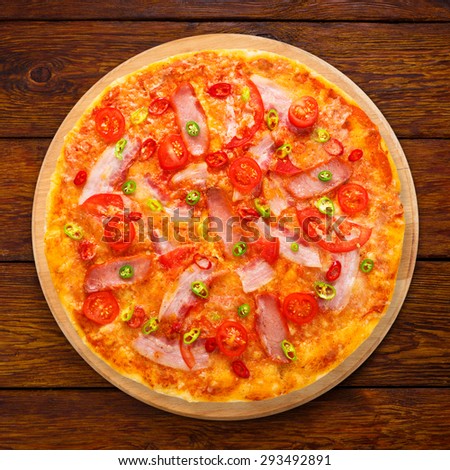 Delicious pizza with red and green hot chili peppers, bacon and cherry tomatoes - thin pastry crust at wooden background above view on wooden desk