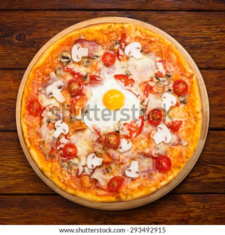 Delicious pizza with mushrooms, bacon, cherry tomatoes and egg - thin pastry crust at wooden background above view on wooden desk