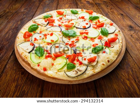 Delicious italian vegetarian pizza with cherry tomatoes, peppers, aubergines and zucchini - thin pastry crust at wooden table background
