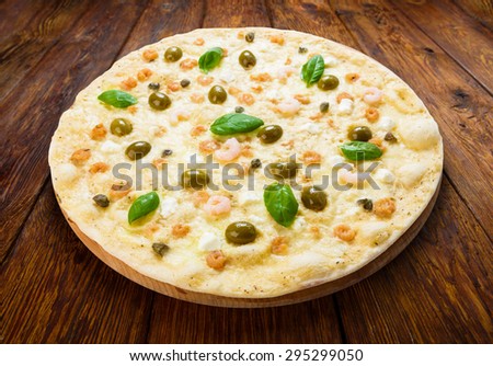Delicious seafood pizza with shrimps, calamari rings, capers and olives - thin pastry crust at wooden table background