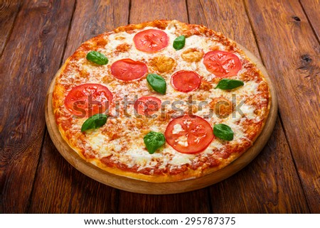 Delicious italian Margherita pizza with tomatoes and mozarella - thin pastry crust at wooden table background on wooden desk