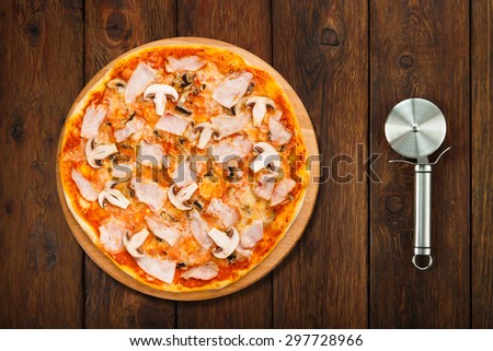 Delicious pizza with mushrooms and smoked chicken meat - thin pastry crust isolated at wooden background  with stainless steel cutter, above view