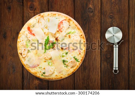 Delicious pizza with chicken, parmesan, tomatoes, white sause and fresh arugula - thin pastry crust isolated at wooden background with stainless steel cutter, above view