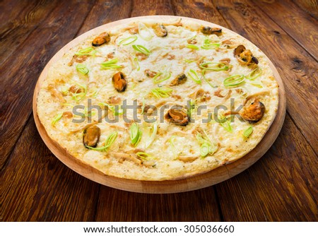 Delicious seafood pizza with shrimps, mussel, olives and leek - thin pastry crust at wooden background
