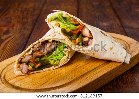 Mexican restaurant fast food - wrapped burritos with chicken and vegetables closeup at wooden desk on table