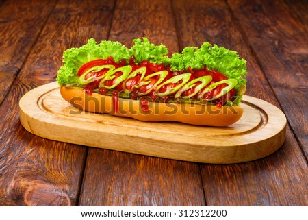 American fast food restaurant cuisine - spicy chili hot dog with mustard, mayonnaise and ketchup with lettuce at wooden desk on the table