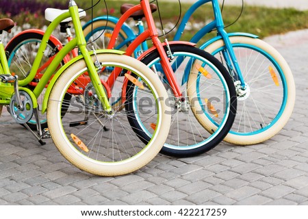 Three beautiful lady city bright colored bicycles or bikes for woman standing in the summer park outdoors, wheel closeup