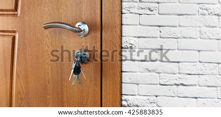 Closed door handle. Door lock with keys. Brown wooden door closeup at white brick wall. Modern interior design, door handle. New house concept. Real estate.