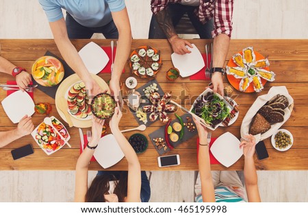 People eat healthy meals at festive table served for party. Friends celebrate with organic food on wooden table top view. Woman pass dish plate to man