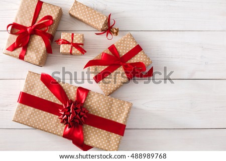 Top view of various gift boxes on white wood background. Presents in craft paper decorated with red ribbon bows. Christmas and other holidays concept, top view with copy space.