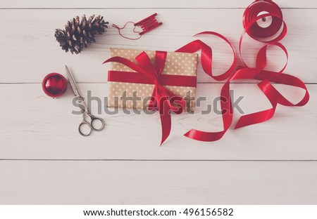 Creative diy hobby. Handmade tools for gift wrapping, christmas present, box in craft paper with red ribbon. Top view of white wooden table with copy space, holiday decoration.