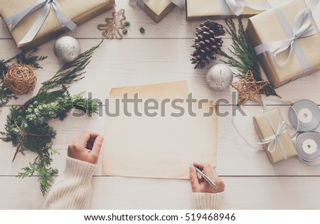 Winter holidays background. Gift wrapping and decorating christmas present, boxes in craft paper with satin silver ribbon. Top view of hands on white wood table sign greeting card, copy space